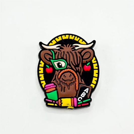 A silicone bead featuring a cartoon illustration of a Highland Cow with glasses and a book, predominantly brown in color with black and yellow accents.

