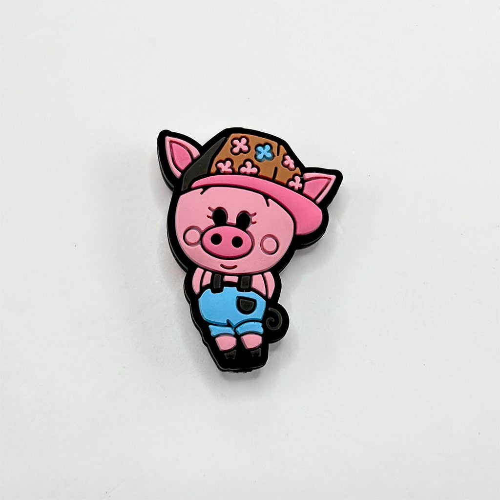 A silicone bead in the shape of a cartoon pig wearing trousers and a brown hat with blue suspenders.

