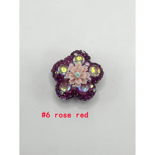 A collection of flower-shaped clay beads with clear rhinestones and solid colors, displayed alongside a beadalon tool.

