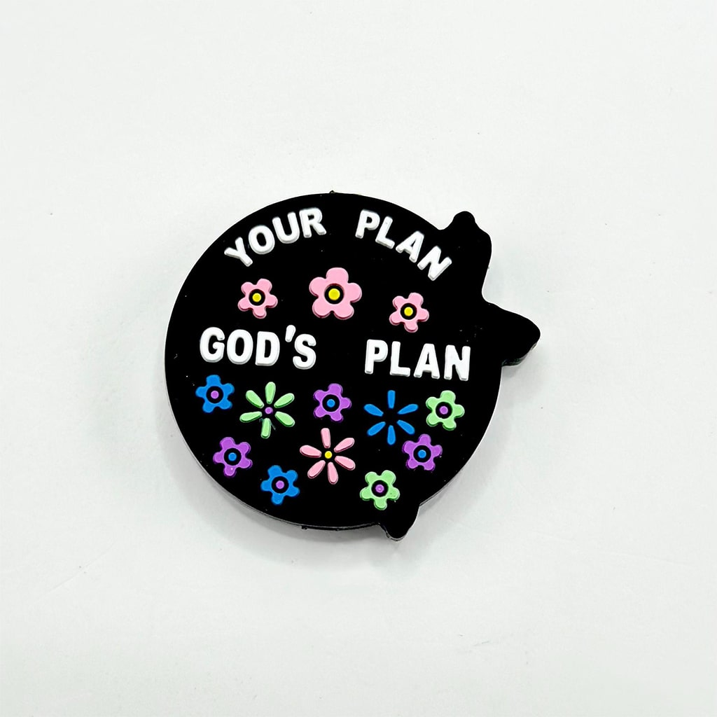 Black fish-shaped pin with 'Your Plan' vs 'God's Plan' text and colorful flowers on a white background

