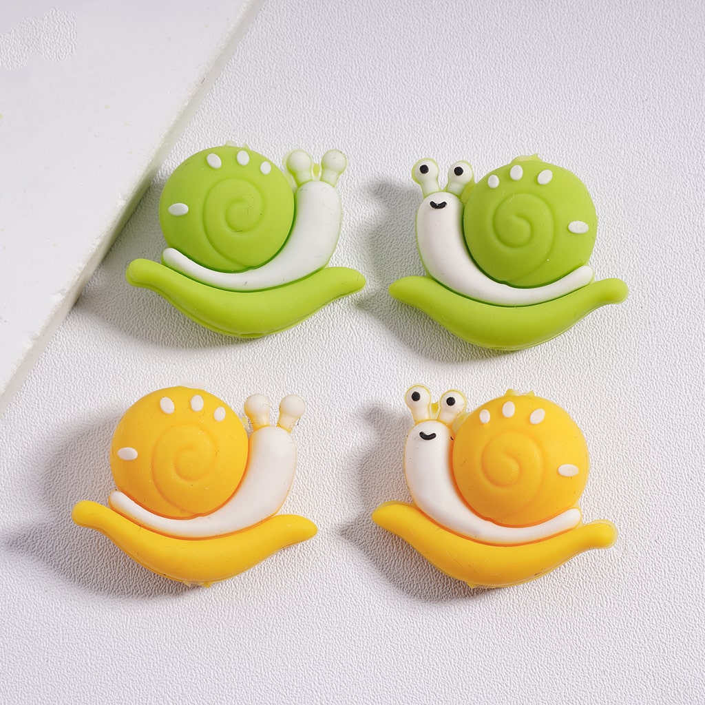 A collection of colorful silicone beads shaped like snails, with two in green and two in orange.

