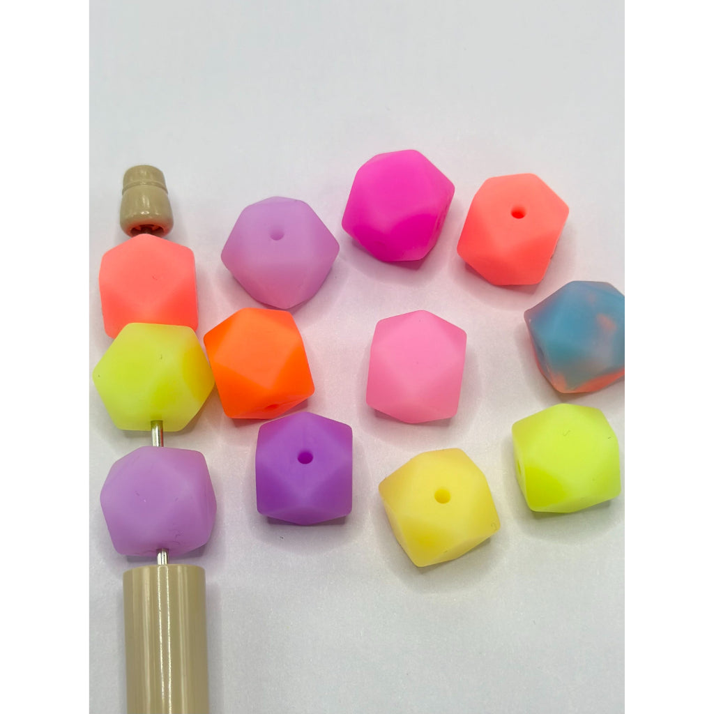 A collection of colorful hexagon-shaped silicone beads laid out on a surface, with visible holes for stringing purposes.

