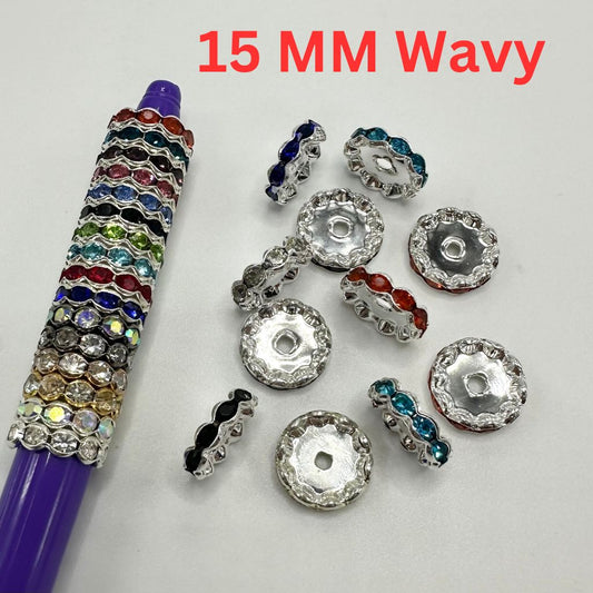 Assorted colorful metal spacers with rhinestones, displayed alongside a purple pen for scale.

