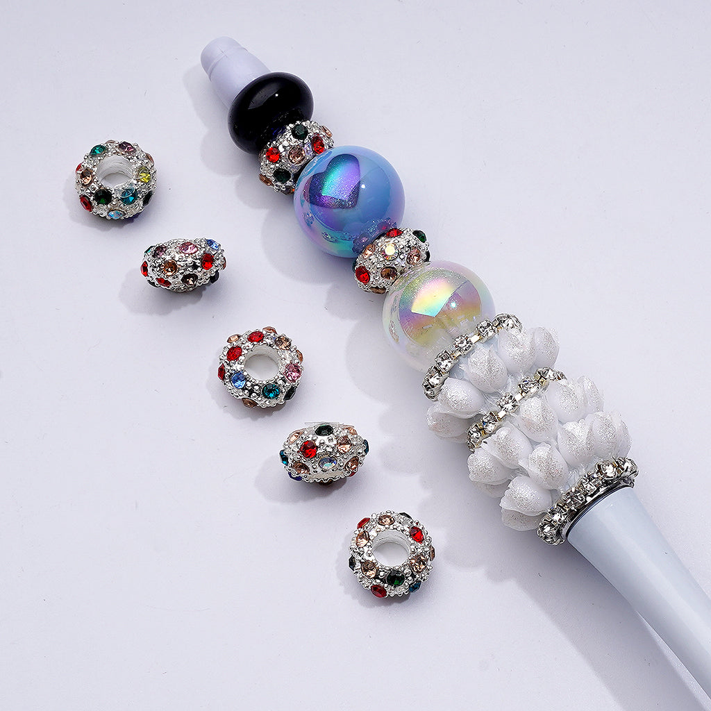 A collection of metal beadable spacers with AB color rhinestones, alongside a bead pen, displayed on a white surface.

