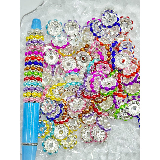 An assortment of colorful wavy shape silver metal spacers with pearls, displayed on a surface.

