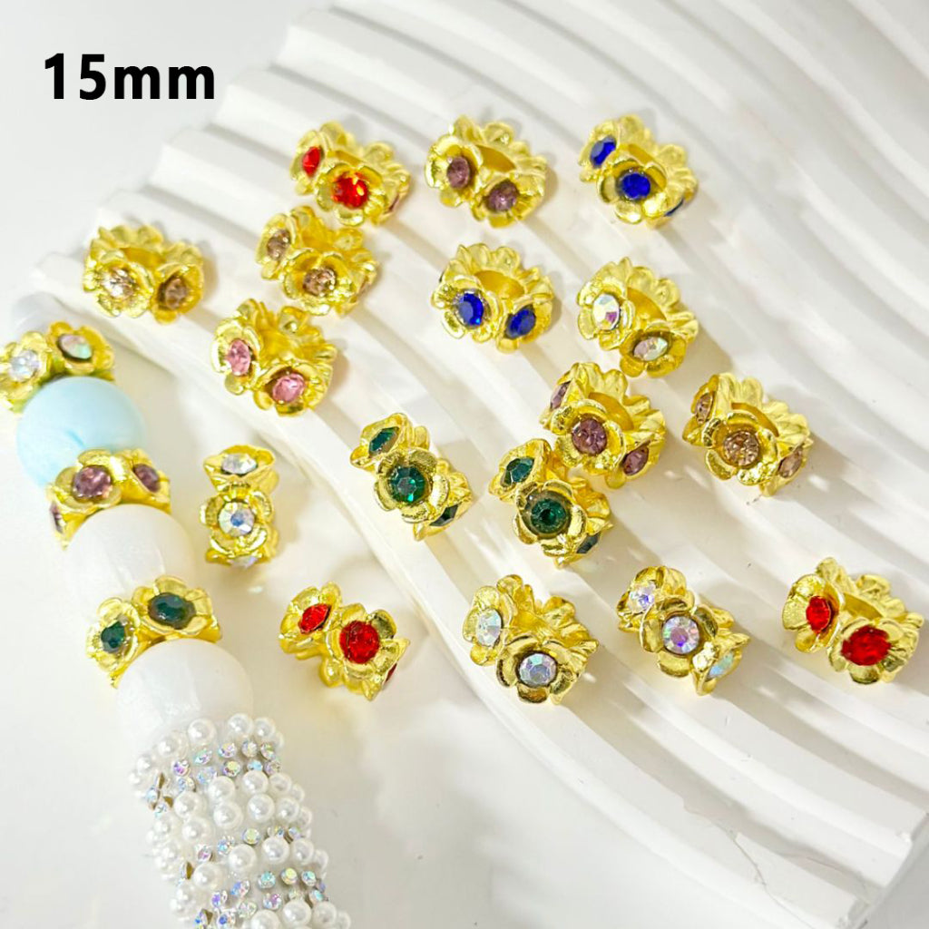 A collection of gold color beadable metal flower spacers with colorful rhinestones, displayed on a white surface.


