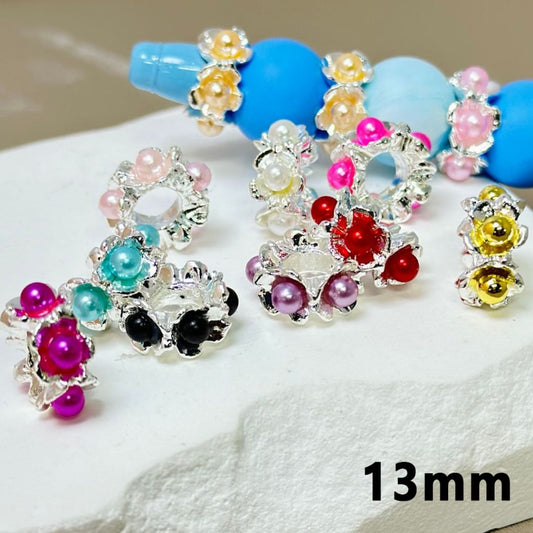 An assortment of silver metal alloy flower spacers with colorful pearls inside, displayed on a surface.

