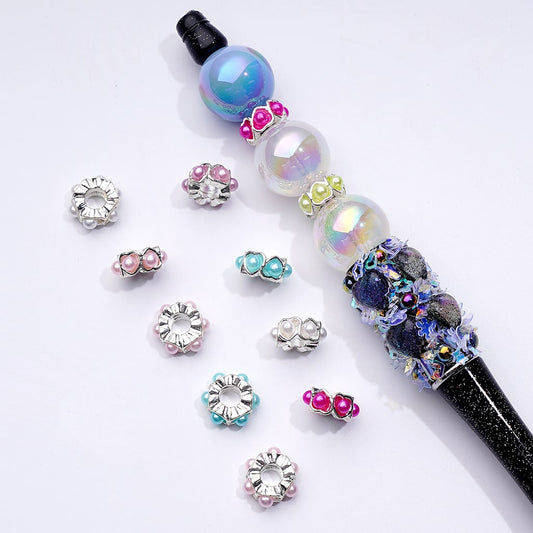 A collection of silver metal heart-shaped spacers with multi-color pearls, displayed alongside a beadable pen.

