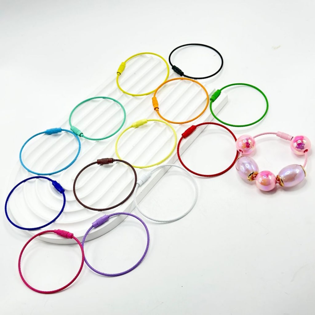 A collection of colorful beadable metal keychain ring loops, some with beads attached, displayed on a white background.

