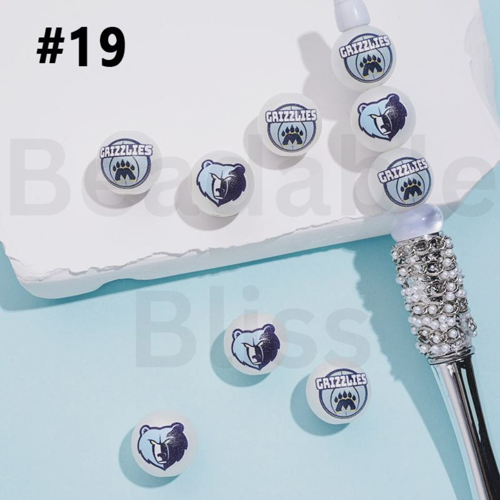 Grizzlies logo earrings on a light blue background with a white box and decorative object.

