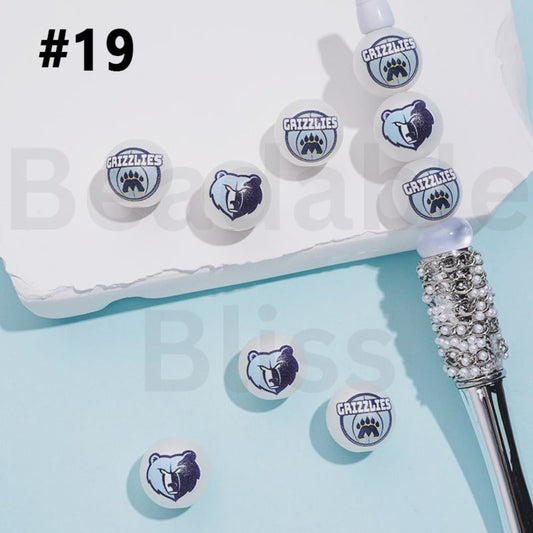 Grizzlies logo earrings on a light blue background with a white box and decorative object.

