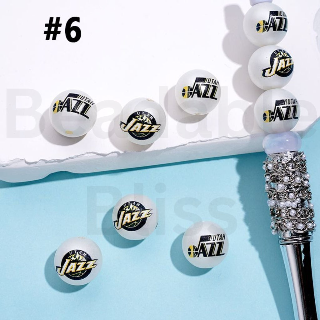 Utah Jazz branded ping pong balls on a blue surface with a decorative pen.

