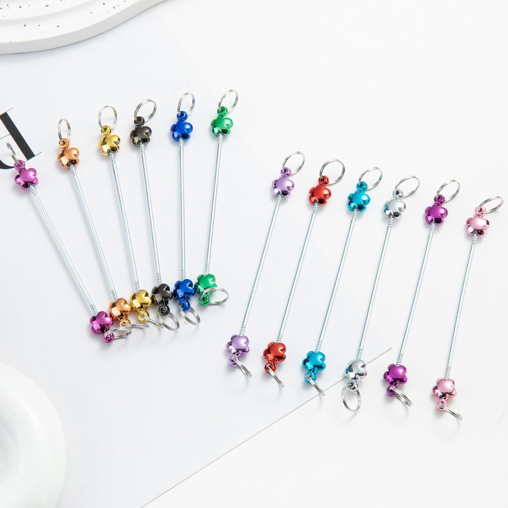 A collection of metallic color beadable keychain bars with flower designs, displayed in a fanned arrangement on a white surface.

