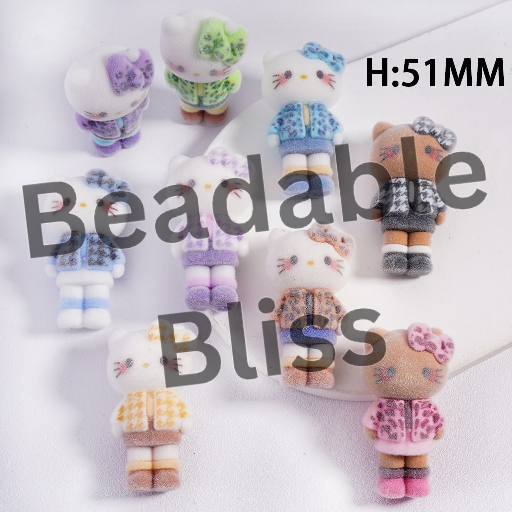 Small plush toys with various outfits on a white surface, branded 'beadablebliss'.