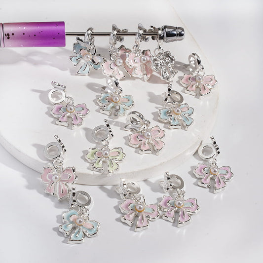 Set of silver charms with pink and blue floral designs on a white surface.

